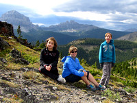 Amy, Sharon, and Riley take cover from the fierce winds in the saddle between McGillivray's south end and the ridge leading to the true summit. Crowsnest Mountain and Seven Sisters are behind them.